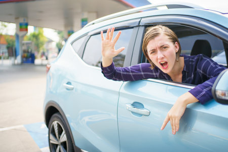 Aggressive young female driver showing a middle finger to other people while driving a car. Woman car driver opened side window and shouting and showing middle finger to camera.の写真素材