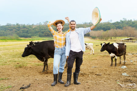 Happy male and female livestock farmer or dairy farmer portrait with a dairy cows in background. Livestock agriculture and farming industry concept.の写真素材