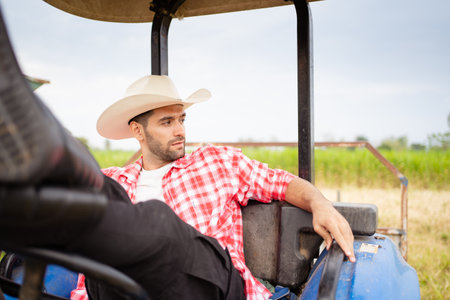 Handsome Middle East Asian man sitting on tractor and relaxing. Male farmer wearing a hat and relaxing on tractor.の写真素材