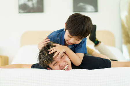 Happy Asian people family, a lovely little young boy playing with father in bedroom together. Father and son playing in bedroom.の写真素材