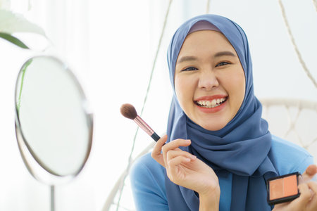 Modern lifestyles of female muslim people portrait, a beautiful Asian muslim woman applying a cosmetic and brushing her face. Modern muslim lifestyle concept.の写真素材