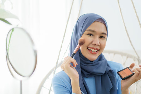 Modern lifestyles of female muslim people portrait, a beautiful Asian muslim woman applying a cosmetic and brushing her face. Modern muslim lifestyle concept.の写真素材