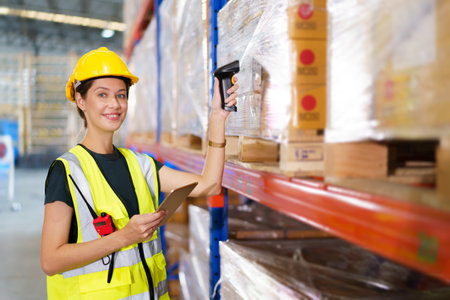 Happy cheerful caucasian white female warehouse worker using laser barcode reader to scan stock inventory in warehouse. Professional occupation in logistic industrial concept.の写真素材