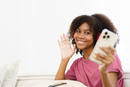 Happy cheerful African - American black woman playing in living room and making a live video or steaming on social media by using smartphone. Woman performs a guitar and makes live video steaming.の写真素材