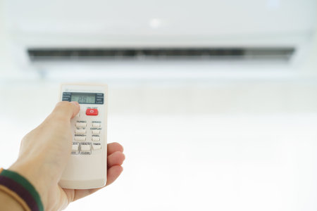 Unrecognizable man using remote control to turn air conditioner on. Man holding an air conditioner remote control and pressing on the temperature control Button.の写真素材