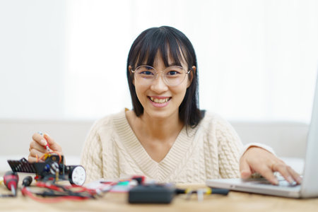Happy cheerful Asian ethnicity female university student learning about robotic and programing by herself, woman assemble a robot and coding.の写真素材
