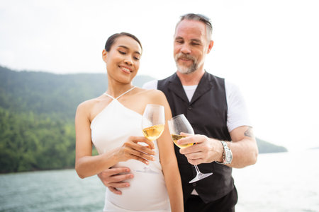 Happy Asian and caucasian white couple celebrating their marriage anniversary together on the yacht. Adult couple sailing a yacht and drinking a Champaign together during a honeymoon trip.の写真素材