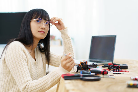Happy cheerful Asian ethnicity female university student learning about robotic and programing by herself, woman assemble a robot and coding.の写真素材