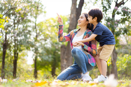 Asian woman and boy playing and walking around the park together with beautiful bokeh and lighting background copyspace. Little cute boy hogging his mother from back and kissing.の写真素材