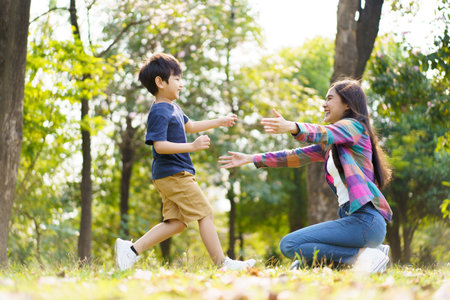 Asian little cute boy running to hug his mother at the park, mother and sun relaxation activity in a park or garden in weekend. Woman and a boy playing on a beautiful sunlight and bokeh background.の写真素材