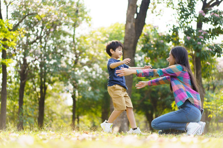 Asian little cute boy running to hug his mother at the park, mother and sun relaxation activity in a park or garden in weekend. Woman and a boy playing on a beautiful sunlight and bokeh background.の写真素材
