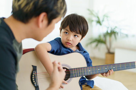 Asian little boy playing an acoustic guitar with his father, a man teaching and playing a guitar with his son in weekend. Happy family - fatherhood concept. Dad teaches his son play a guitar.の写真素材