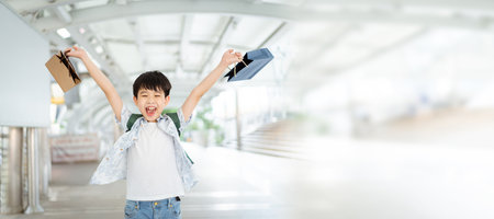 Cheerful happy Asian little boy carrying a paper shopping bags and smiling to camera.の写真素材