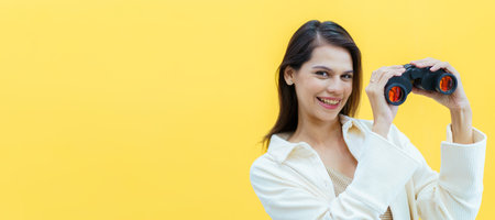 Beautiful caucasian white young woman looking through the twin lens binocular. Woman using binocular portrait on yellow background.の写真素材