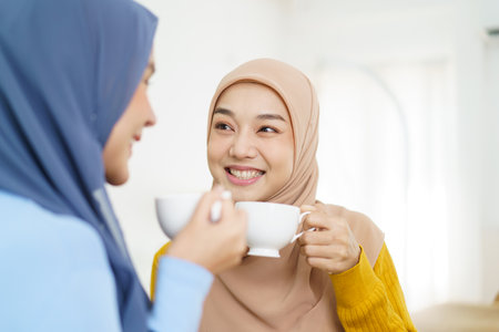 Happy cheerful Asian muslim women drinking a tea or coffee together in the living room and having a business discussion. Modern muslim people lifestyle concept.の写真素材