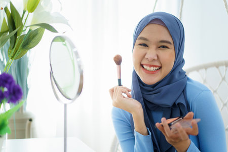 Modern lifestyles of female muslim people portrait, a beautiful Asian muslim woman applying a cosmetic and brushing her face. Modern muslim lifestyle concept.の写真素材