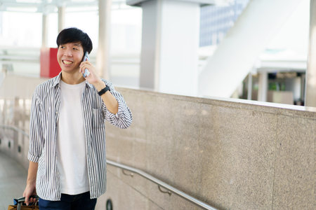 Asian young man dragging a suitcase along the city or airport terminal with shopping bags. Man traveling in the city or urban area.の写真素材