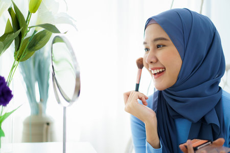 Modern lifestyles of female muslim people portrait, a beautiful Asian muslim woman applying a cosmetic and brushing her face. Modern muslim lifestyle concept.の写真素材