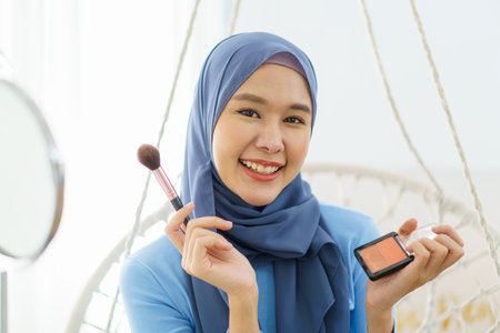 Modern lifestyles of female muslim people portrait, a beautiful Asian muslim woman applying a cosmetic and brushing her face. Modern muslim lifestyle concept.の写真素材