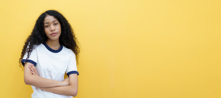 Beautiful American African black woman standing on the yellow background with copyspace. Beautiful young black woman crossed arms and look at camera portrait.の写真素材