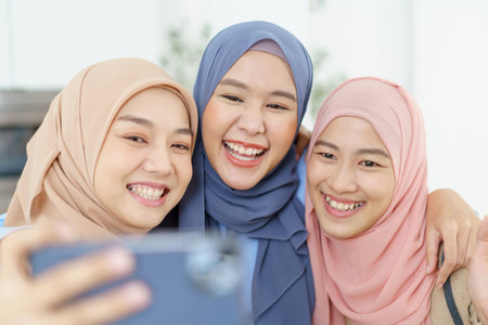 Group of happy cheerful Asian muslim women taking a selfie photography or making video live steaming on a social network by using smartphone.の写真素材