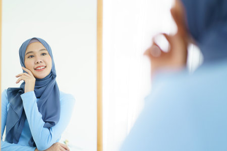 Modern lifestyles of female muslim people portrait, a beautiful Asian muslim woman applying a cosmetic and brushing her face. Modern muslim lifestyle concept.の写真素材