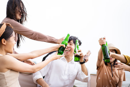 Group of Asian young adult people enjoy drinking a beer together during camping at the park. Asian young women and men celebrating with a bottle of a beer together.の写真素材