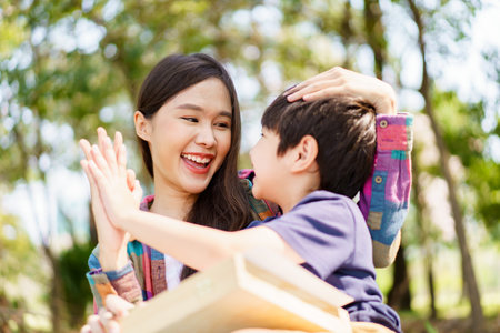 Happy cheerful Asian lovely little boy and mother sitting under the tree at park in the morning and drawing a picture. Asian woman spending time in weekend with her lovely little son.の写真素材