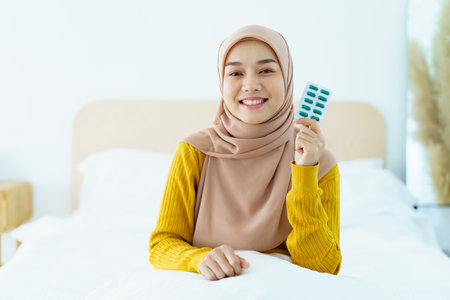 Asian young muslim woman showing a pill and water bottle, muslim woman taking a pill capsule. Health care and wellness in diverse ethnicity people and religious concept.の写真素材