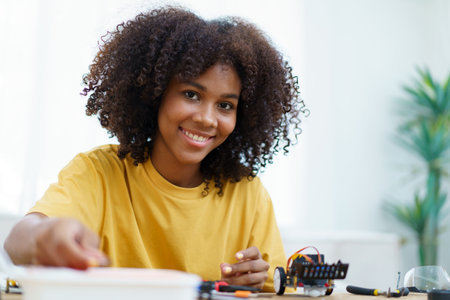 Happy cheerful American - African black ethnicity female university student learning about robotic and programing by herself, woman assemble a robot.の写真素材