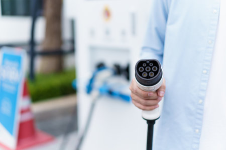 Unrecognizable Asian man holding AC type 2 EV charging connector at EV charging station, man...