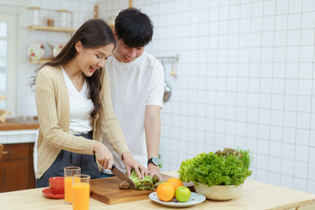 Happy cheerful Asian couple making an organic vegetable salad together in kitchen, woman using cooking knife cut a vegetables. Healthy eating concept.の写真素材