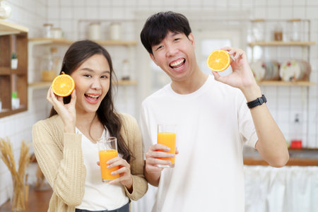 Happy cheerful Asian man and woman showing a half round of a fresh orange fruit to camera together and smiling.の写真素材