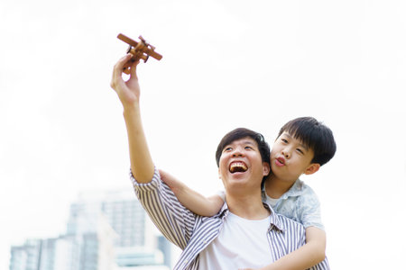 Happy cheerful Asian daddy and little son playing with a wooden air plane toy together, a concept of creativity - education in children learning.の写真素材