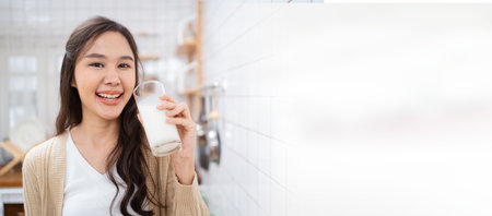 Beautiful happy Asian woman drinking a milk in morning in kitchen and smiling to camera. Happy Asian woman shows a glass of milk and smiles.の写真素材