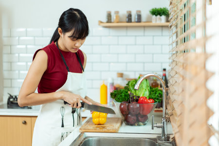 Happy cheerful beautiful Asian woman using cooking knife cutting a vegetables in kitchen. Woman preparing a vegan salad in kitchen.の写真素材