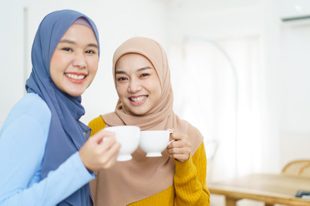 Happy cheerful Asian muslim women drinking a tea or coffee together in the living room and having a business discussion. Modern muslim people lifestyle concept.の写真素材