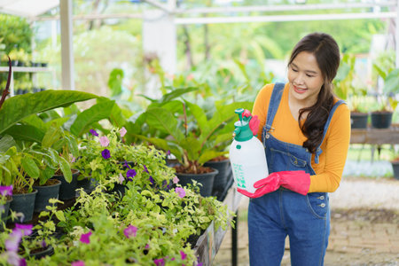 Happy cheerful Asian female botanist or gardener carrying a shovel and water bottle and smile to camera. Beautiful Asian woman planting and watering a small houseplants.の写真素材