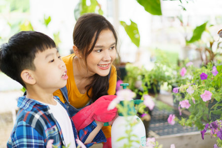 Happy Asian woman and little boy planting a house plants in green house together. Satisfied little boy enjoy planting and watering a small tree with his mother in greenhouse.の写真素材