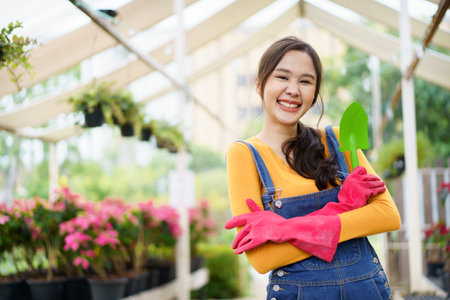 Happy cheerful Asian female botanist or gardener hold a shovel and crossed arm and smile to camera. Beautiful Asian woman planting and watering a small houseplants.の写真素材