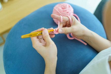 Happy cheerful Asian woman doing a crochet in living room in free time. Skillful Asian craftswoman knitting a handcraft crochet sweater and hat in cozy living room.の写真素材