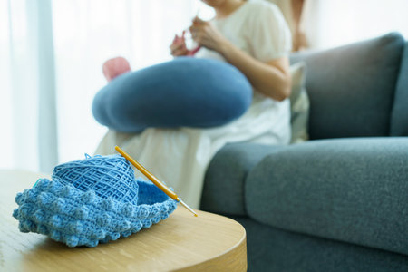 Happy cheerful Asian woman doing a crochet in living room in free time. Skillful Asian craftswoman knitting a handcraft crochet sweater and hat in cozy living room.の写真素材
