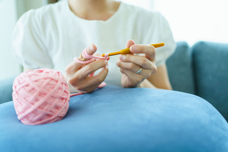 Happy cheerful Asian woman doing a crochet in living room in free time. Skillful Asian craftswoman knitting a handcraft crochet sweater and hat in cozy living room.の写真素材