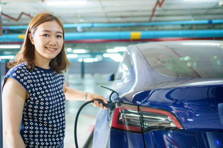 Beautiful Asian woman connecting a AC Type 2 EV charging connector to a vehicle, woman preparing an EV - electric vehicle charging connector for recharge a vehicle.の写真素材