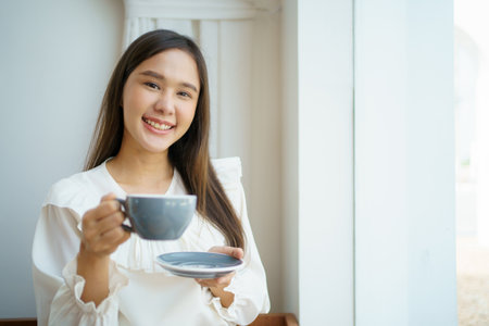 Asian businesswoman holding a coffee cup on hand during relaxing in the coffee shop. Asian smart and good looking businesswoman taking a break in coffee shop.の写真素材