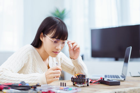 Happy cheerful Asian ethnicity female university student learning about robotic and programing by herself, woman assemble a robot and coding.の写真素材