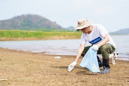 Asian young man picking up a plastic bottle garbage on the beach, male volunteer walking around the beach and collecting - cleaning a plastic waste.の写真素材