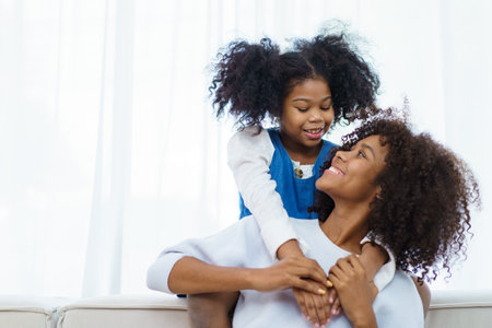 Happy cheerful little American - African ethnicity little girl and mother staying together, mom hugging her daughter.の写真素材