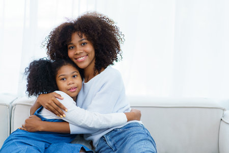 Happy cheerful little American - African ethnicity little girl and mother staying together, mom hugging her daughter.の写真素材