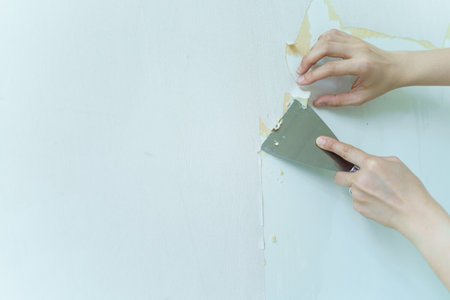 Asian woman fixing and removing a broken wallpaper by herself. Close up angle showing a housewife repairing the broken wallpaper in old house and cleaning a wall to prepare for painting.の写真素材